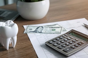 Large model tooth on a desk next to paper, calculator, and money