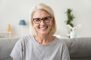 Woman with red glasses and gray t-shirt sitting on sofa smiling