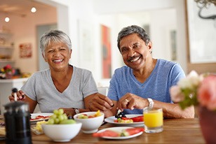 Woman in gray t-shirt sitting at table with man in blue shirt enjoying assorted fruits