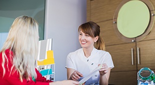 Friendly dental team member talking with patient at front desk