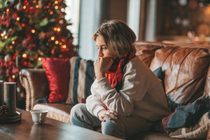 Concerned woman sitting on couch with Christmas tree in background