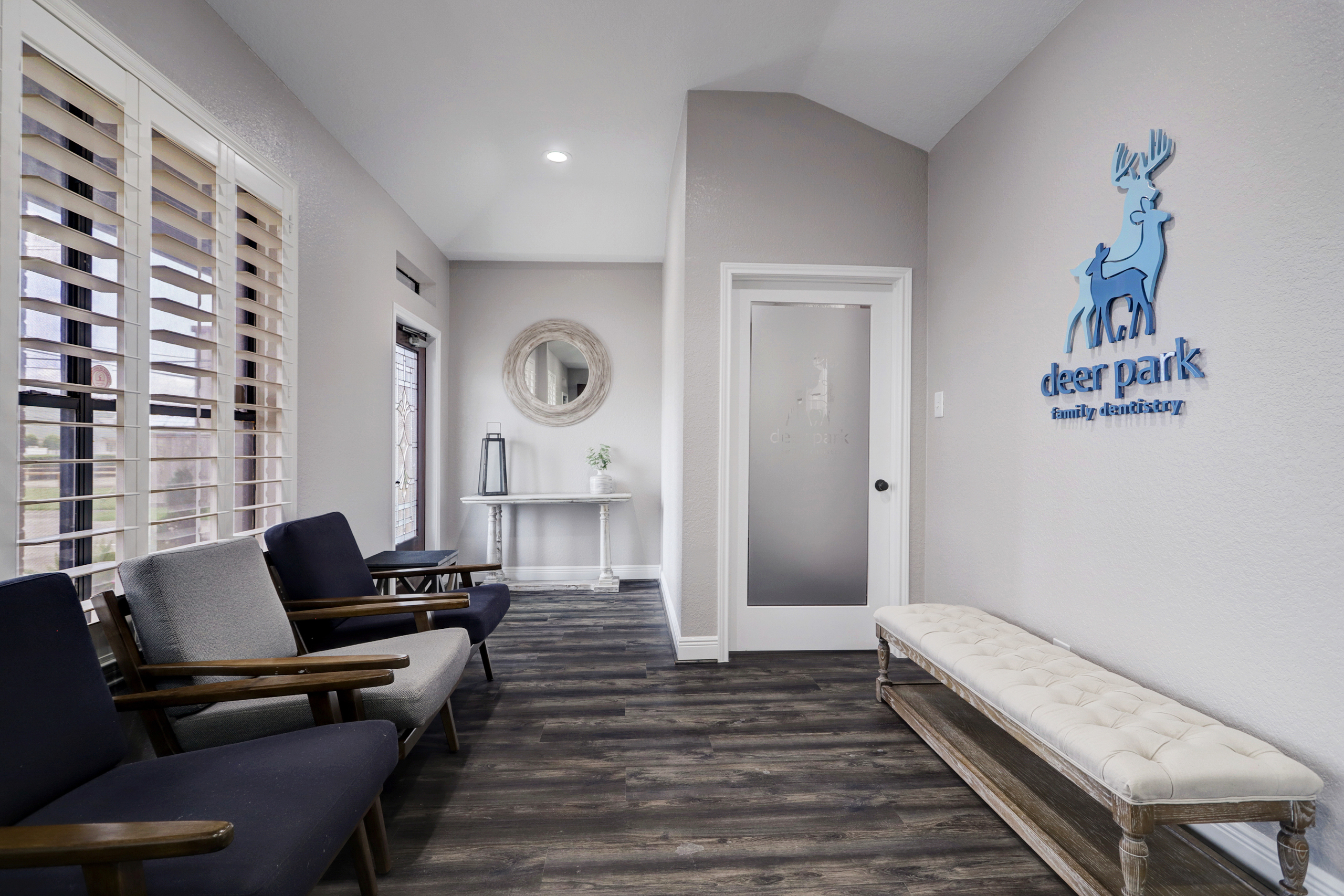 Reception area at Deer Park Family Dentistry featuring cushioned bench seating, modern chairs, hardwood floors, and the practice logo on the wall near the frosted glass door – Deer Park Family Dentistry